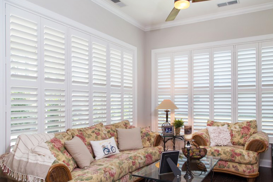 White Polywood shutters behind floral couches in a sunroom